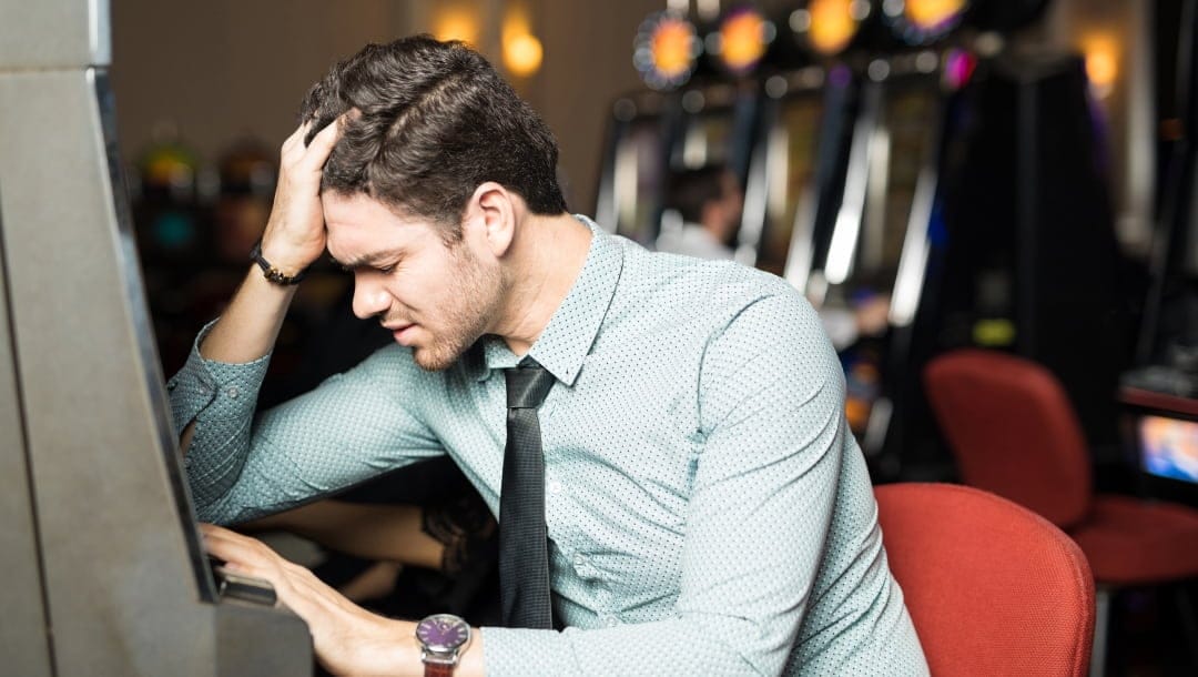 A man at a slot machine experiencing the stress that could be associated with gambling addiction and problem gambling.