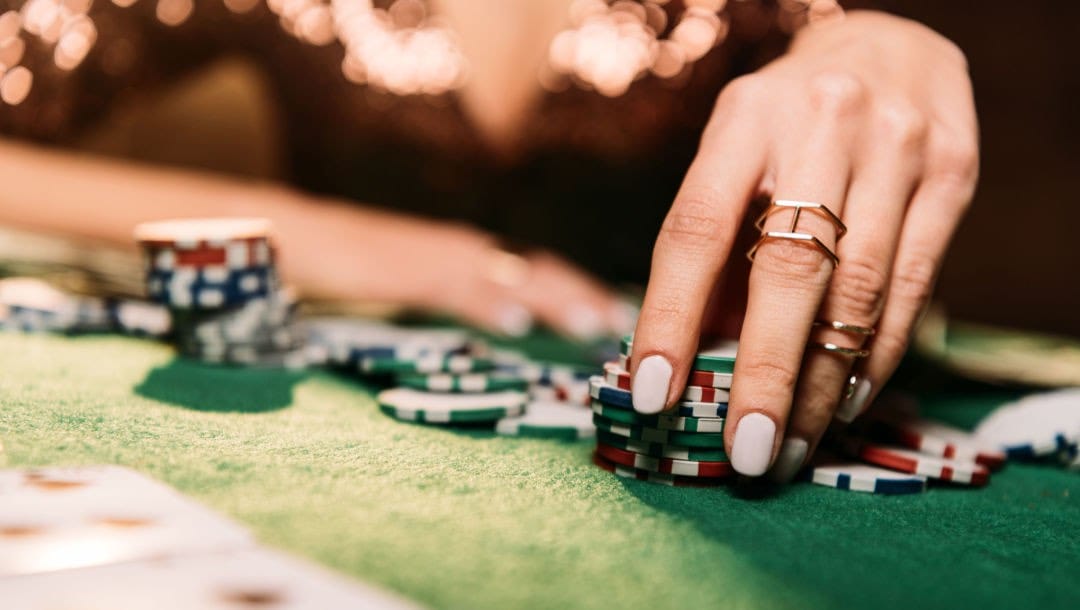 A woman picking up casino chips at a poker table.