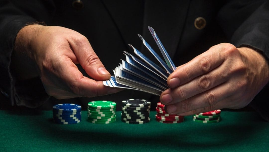 A dealer shuffling cards with poker chips beneath his hands.
