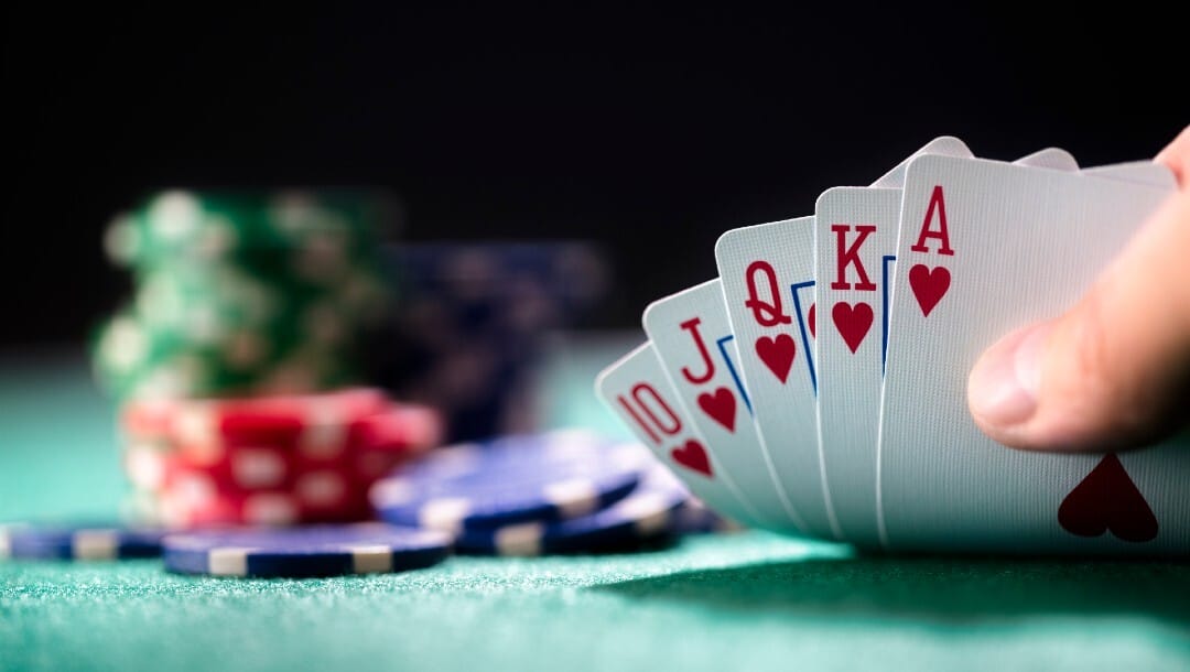 Hand holding a winning royal flush hand of cards with chips on the background