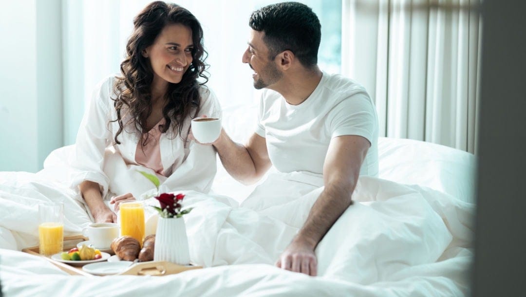 A happy couple having breakfast in bed at a hotel.