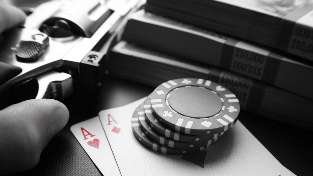 Stacks of cash, casino chips, playing cards and a pistol on a table.