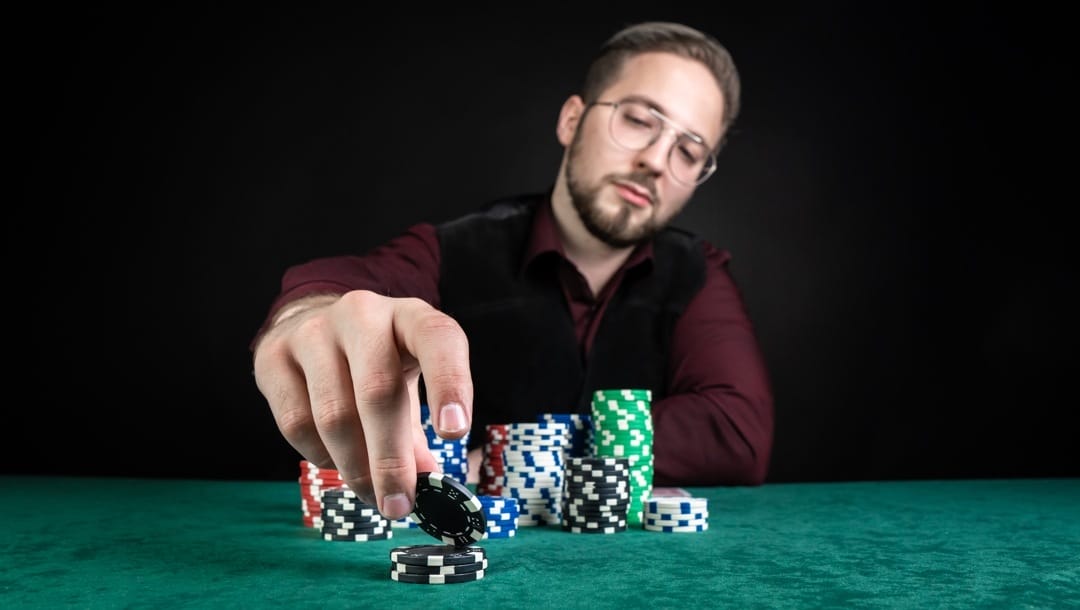 A poker player stacks four black and white poker chips in front of their main chip stack.
