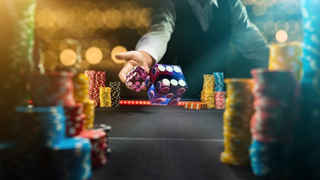 A person rolling a pair of dice on a casino table surrounded by casino chips.