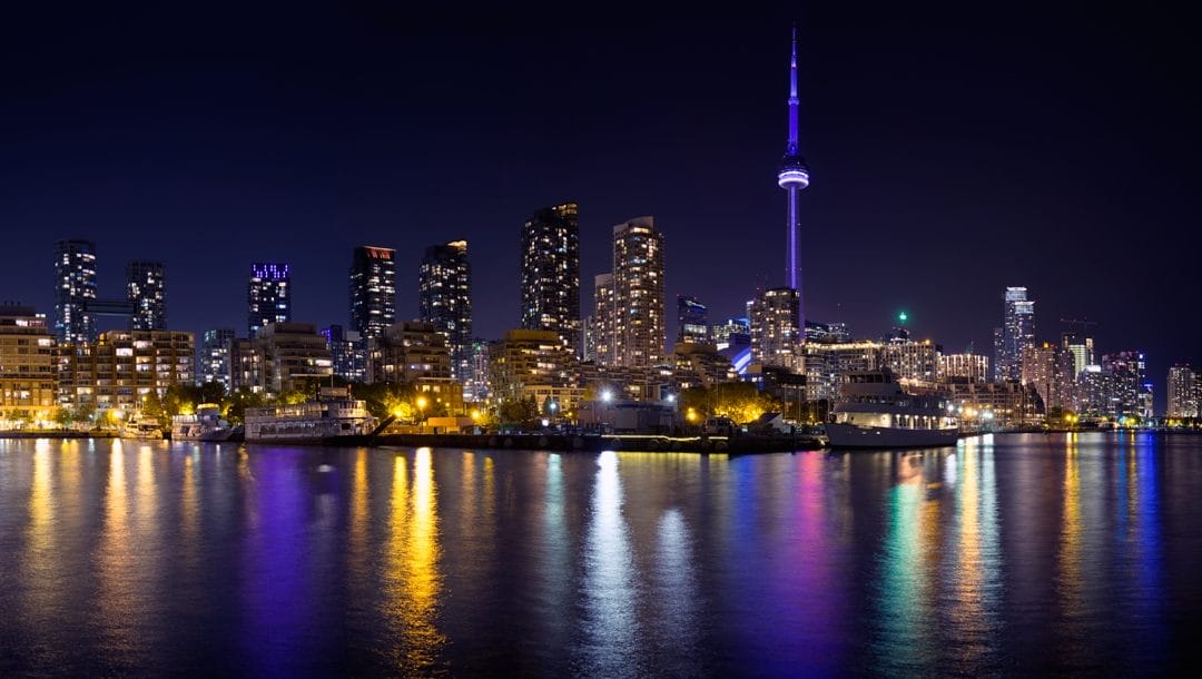 The Toronto skyline at night. The lights from the city are reflected in the waters of Lake Ontario.