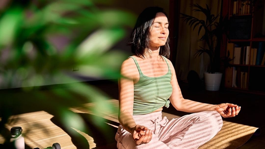A woman surrounded by plants meditating in a quiet room.