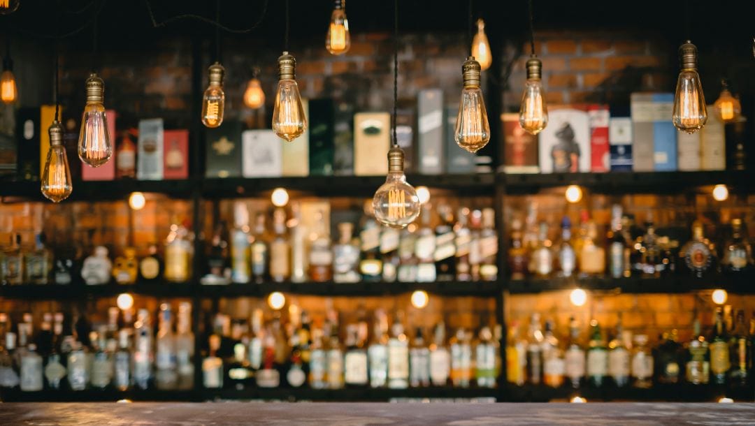 Vintage lamps hanging above a metal counter in front of a well-stocked bar.