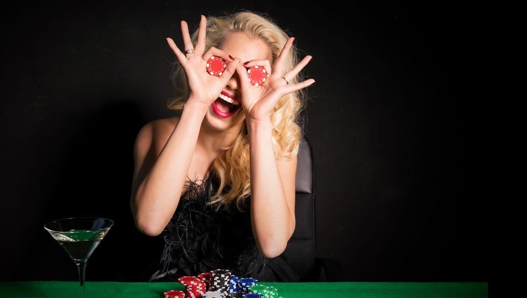 A woman holding poker chips to her eyes in a playful way.