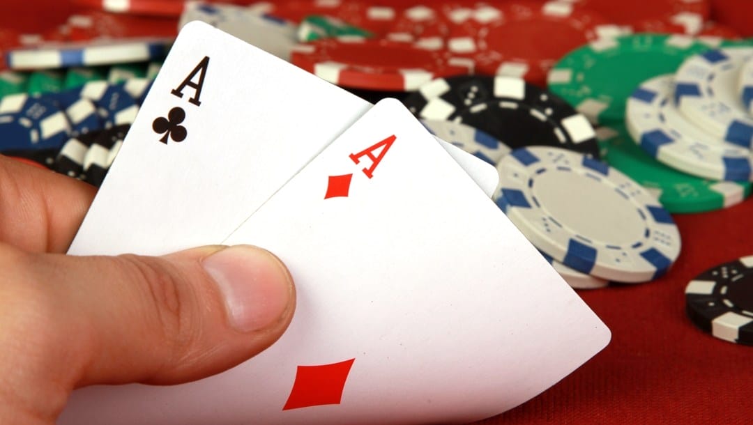 A poker player looks at their hole cards and sees two aces. There are poker chips scattered on the table behind them.