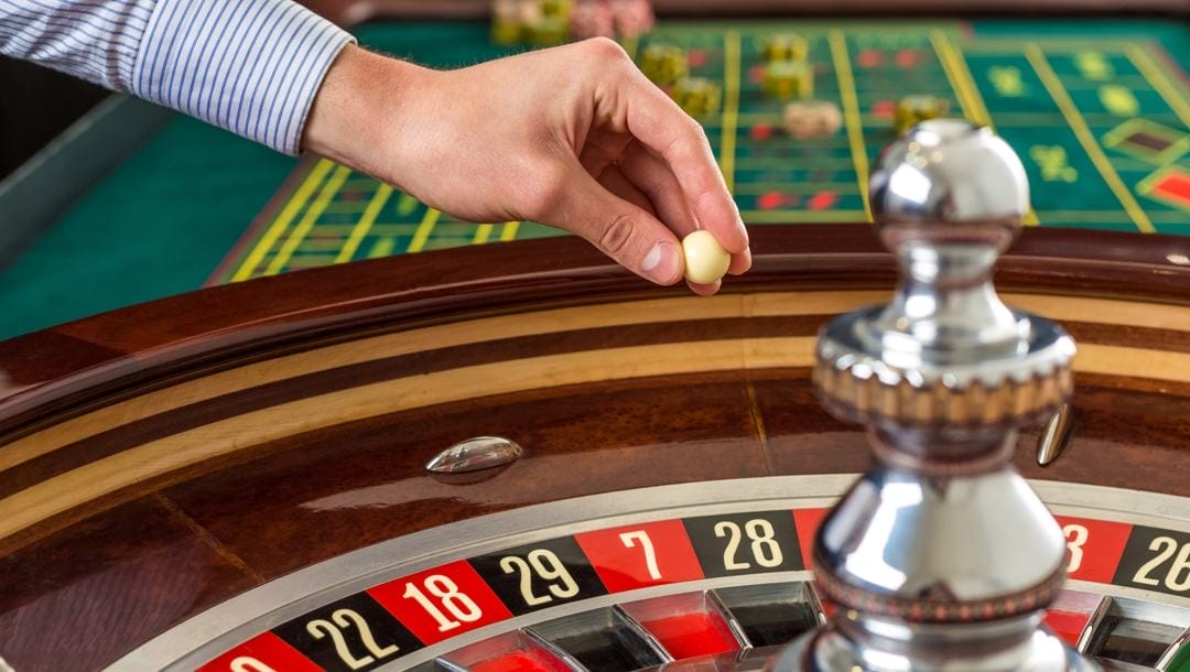 A croupier about to drop a roulette ball into play on a roulette wheel.
