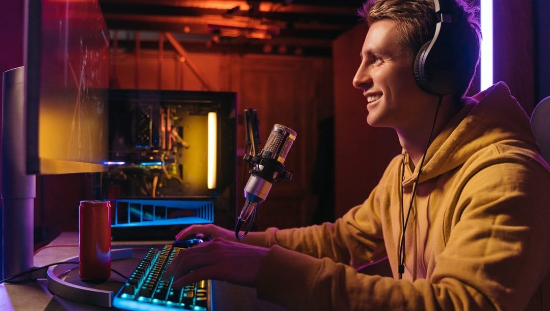 A young adult wearing headphones live-streams on a computer.