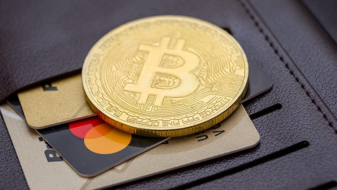 A coin with the Bitcoin symbol sits on various credit cards in a wallet.