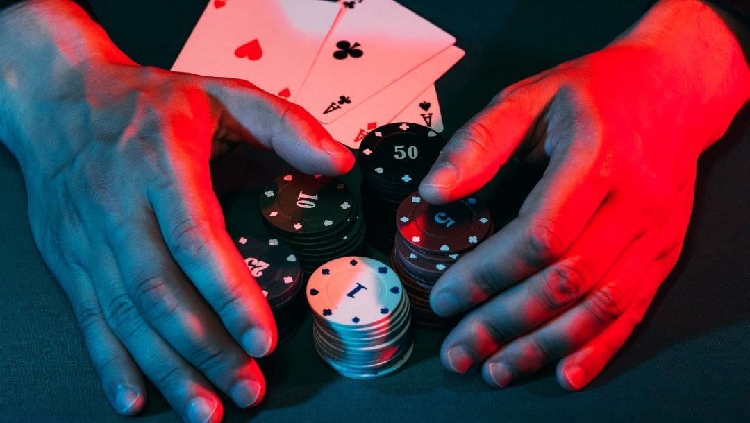A man’s hand claiming poker chips with a winning hand of four aces