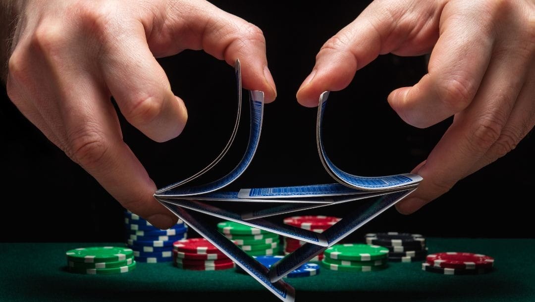 A man’s hands shuffling playing cards in front of a stack of poker chips on a poker table