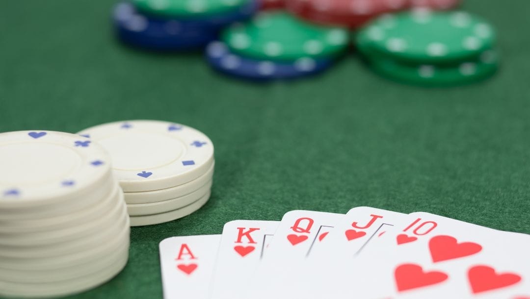 a winning hand of Royal Flush of hearts on a green poker table surrounded by poker chips