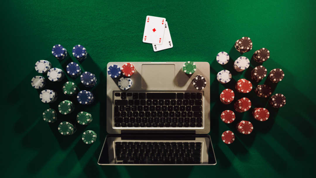 Aerial view of a laptop with poker chips and two cards on a table