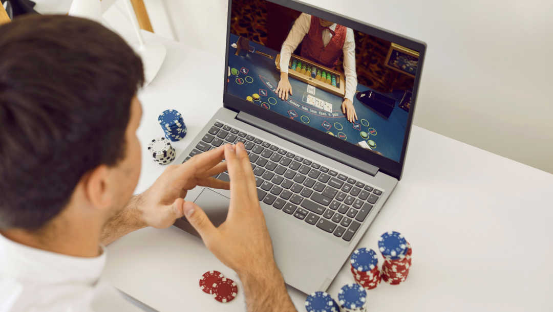 A man playing online poker at a desk with some poker chips on the table