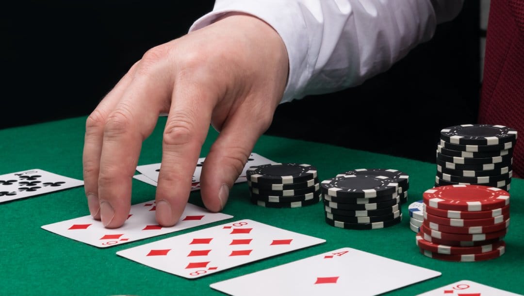 A poker dealer touches a playing card on a poker table.