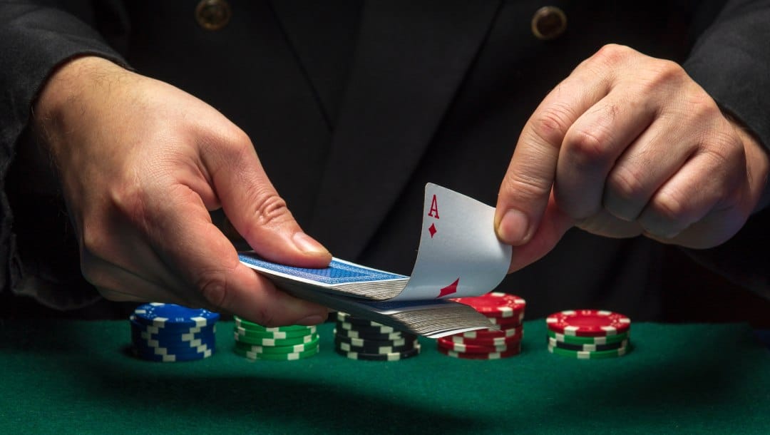 A croupier pulls an ace from a deck of cards over a green felt table with poker chips.