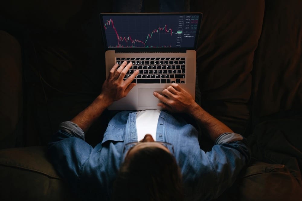Top view of a man sitting on a couch looking at stocks on laptop.