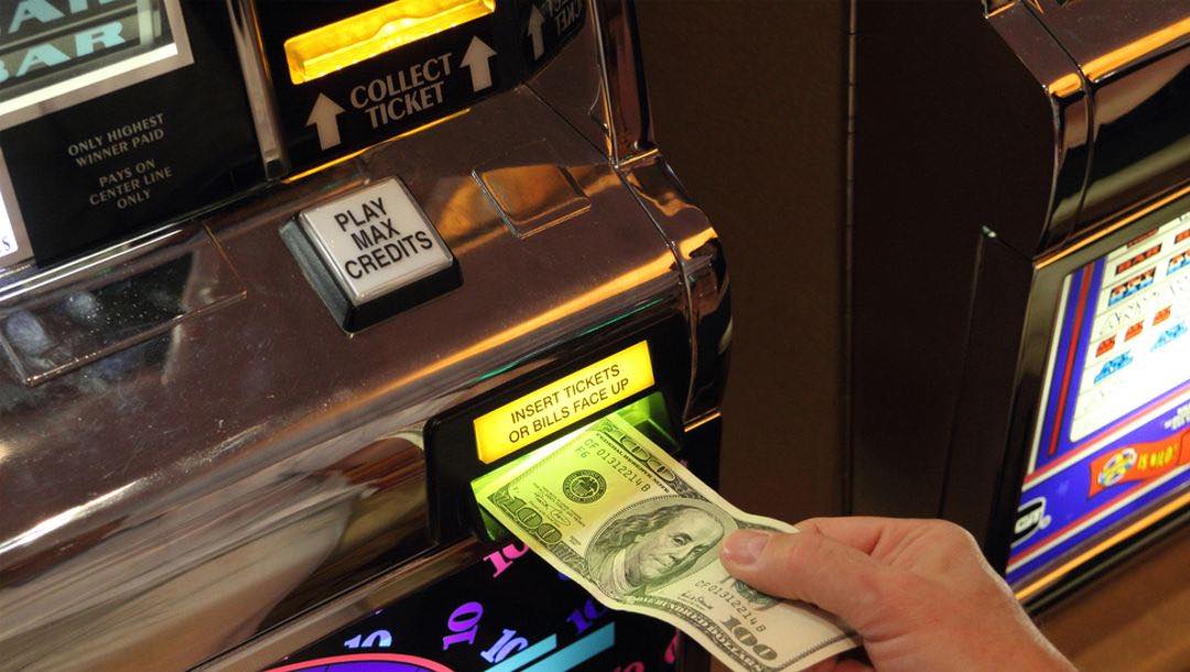 A casino player inserting a $100 dollar bill into a game machine.