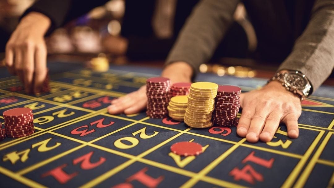 a man resting his hands on a roulette number table on either sides of stacks of poker chips in a casino