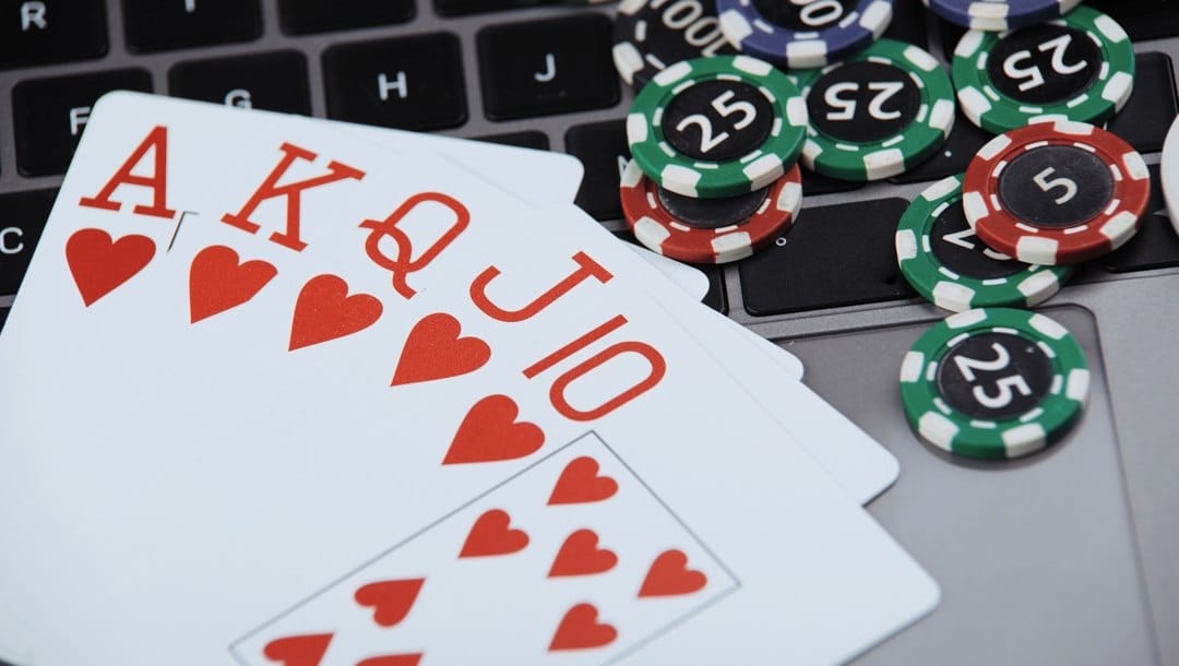 A royal flush on a laptop keyboard next to scattered poker chips.