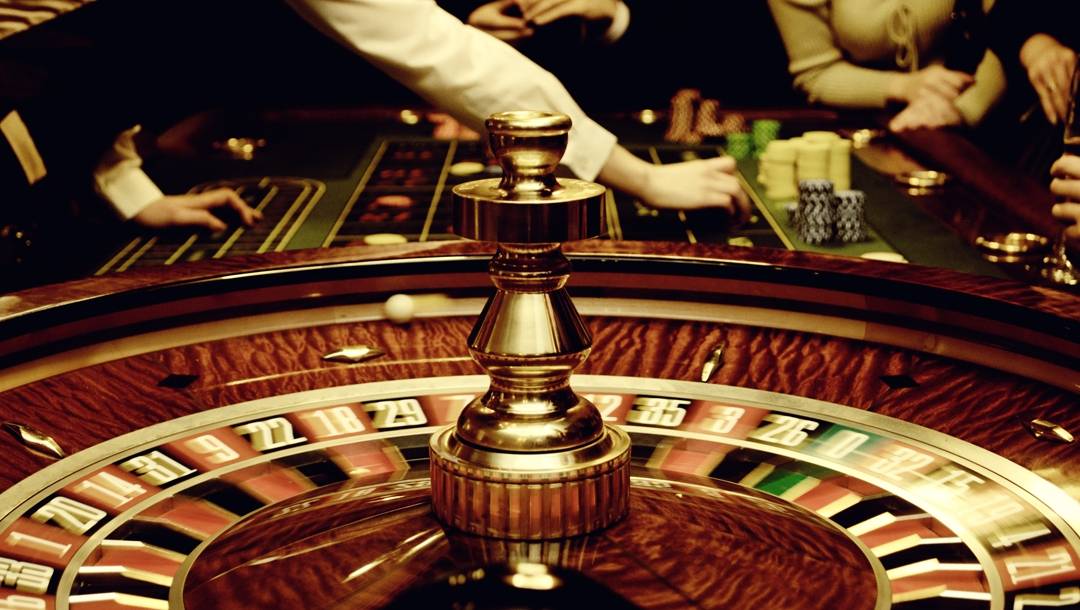 A spinning roulette wheel in front of a dealer finalizing bets in the background.