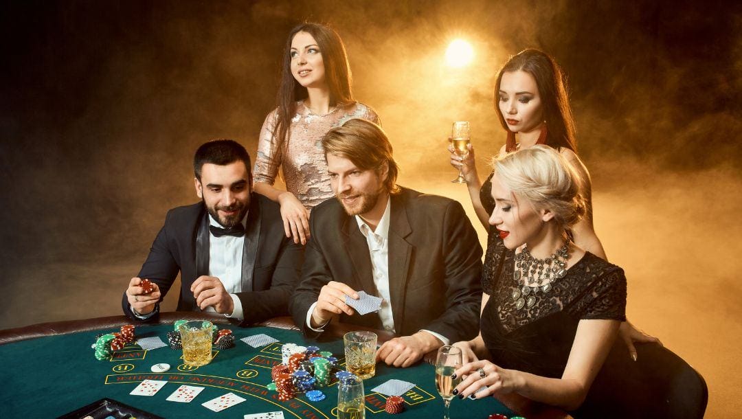 five people standing around a blackjack poker table playing blackjack and drinking