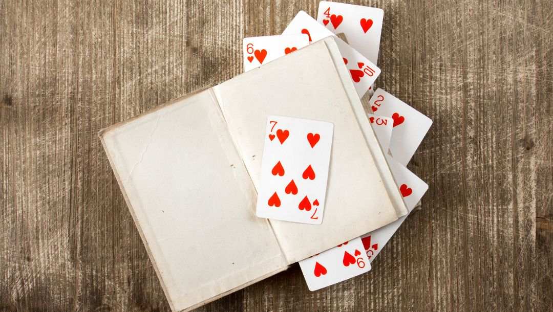 A blank open book on a wooden table with playing cards sticking out of the pages