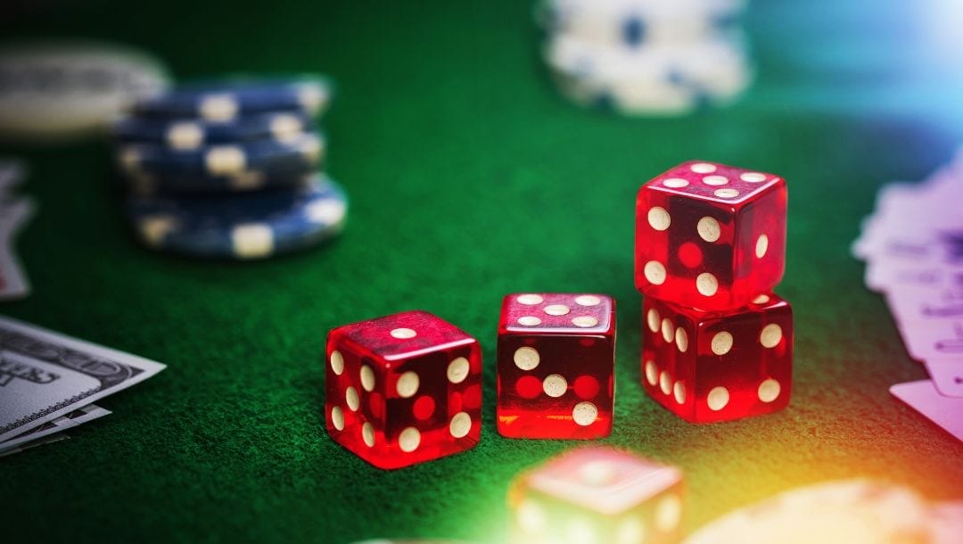 red dice on a green felt poker table surrounded by poker chips, money and playing cards