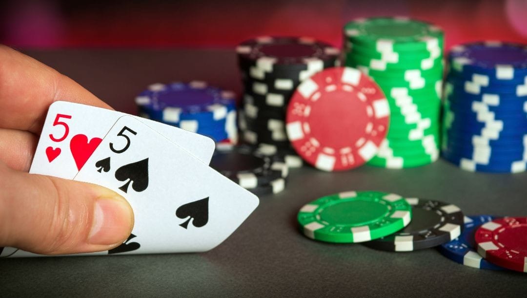 Header image, a man looks at his hole cards, a pocket pair of fives, next to stacks of poker chips
