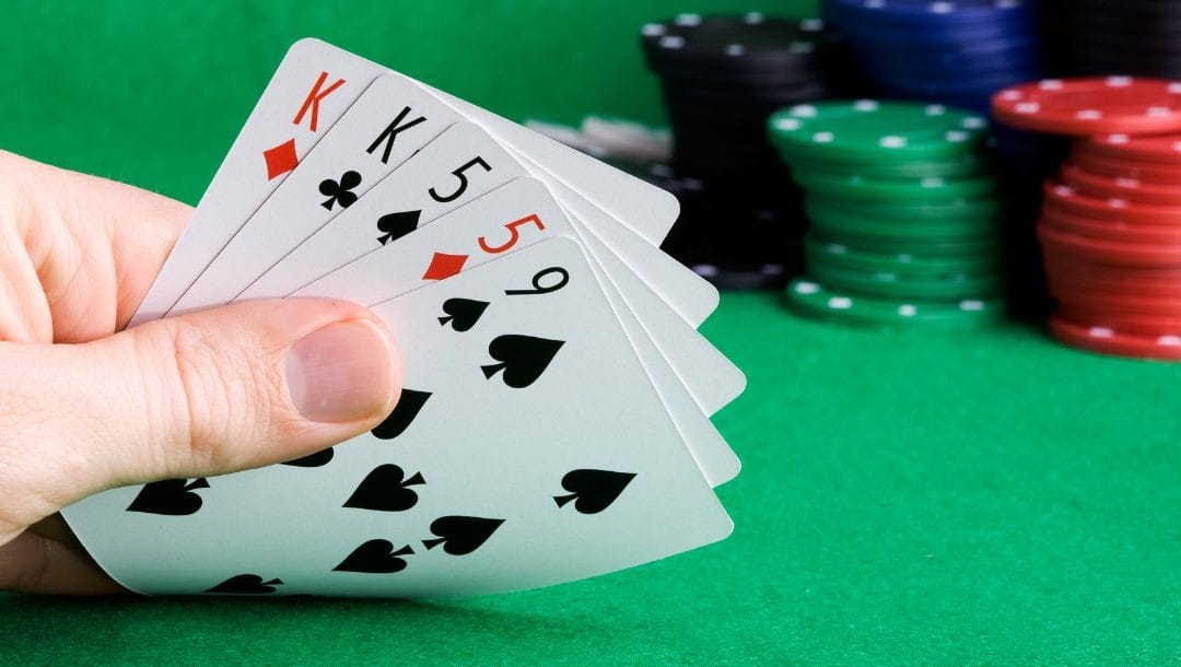 a hand of five playing cards on a green felt poker table with poker chips stacked behind