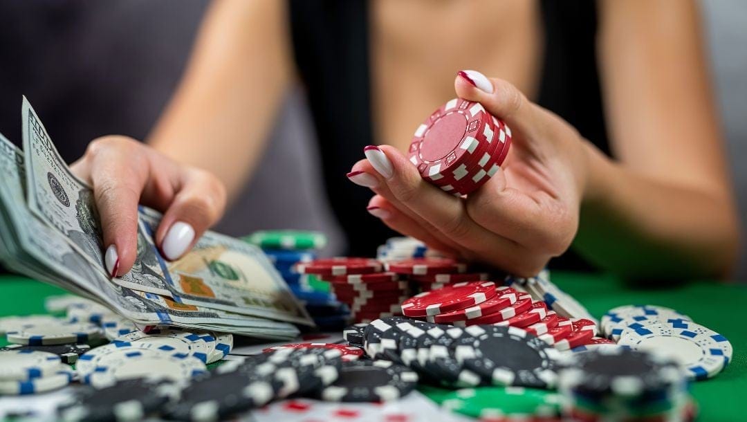 a woman sitting at a green felt casino poker table with a pile of poker chips and a handful of money