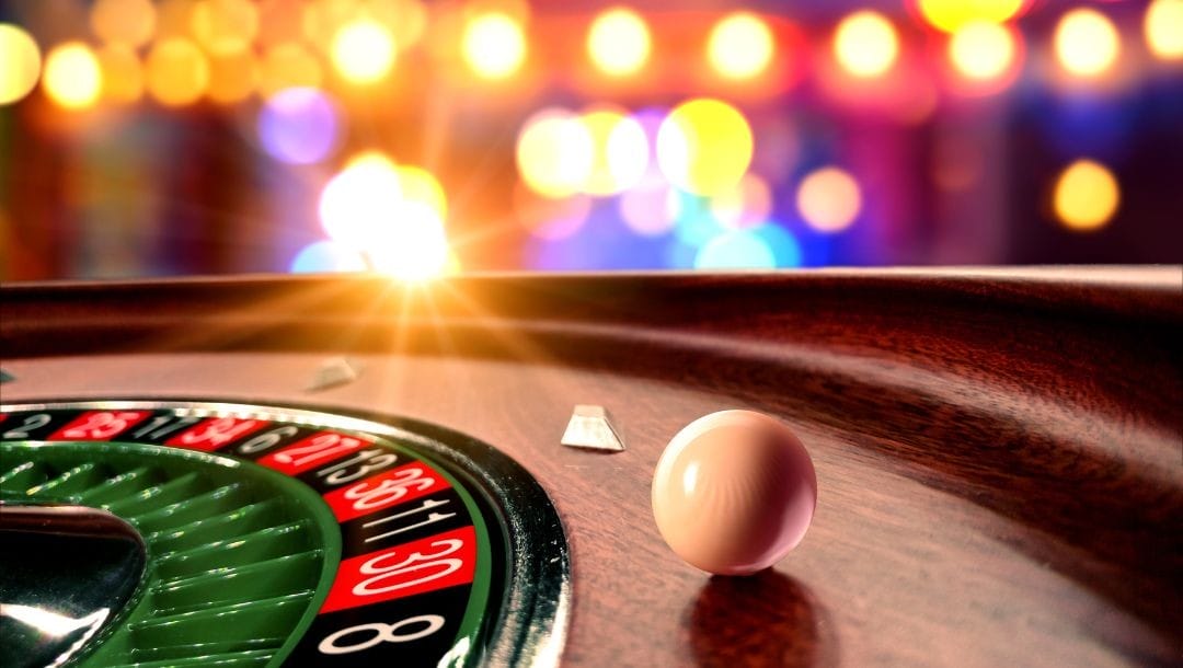 Header image, closeup of roulette wheel with white roulette ball spinning, bright lights stream in the background