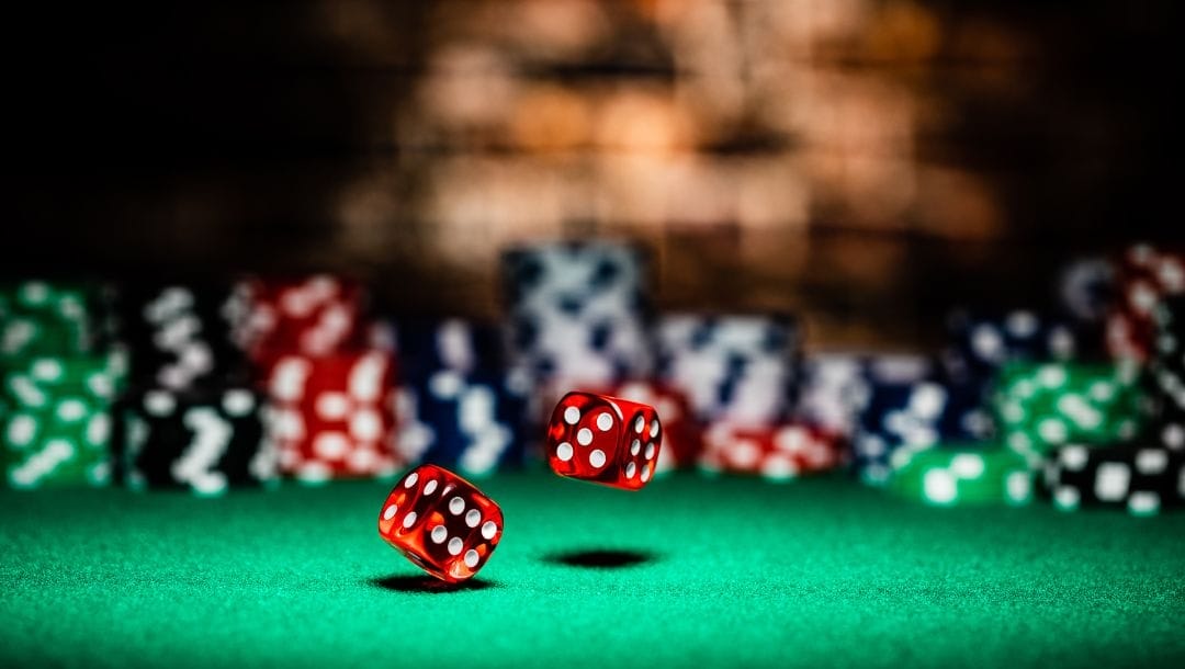 two red dice bouncing on a green felt surface with stacks of poker chips in the background