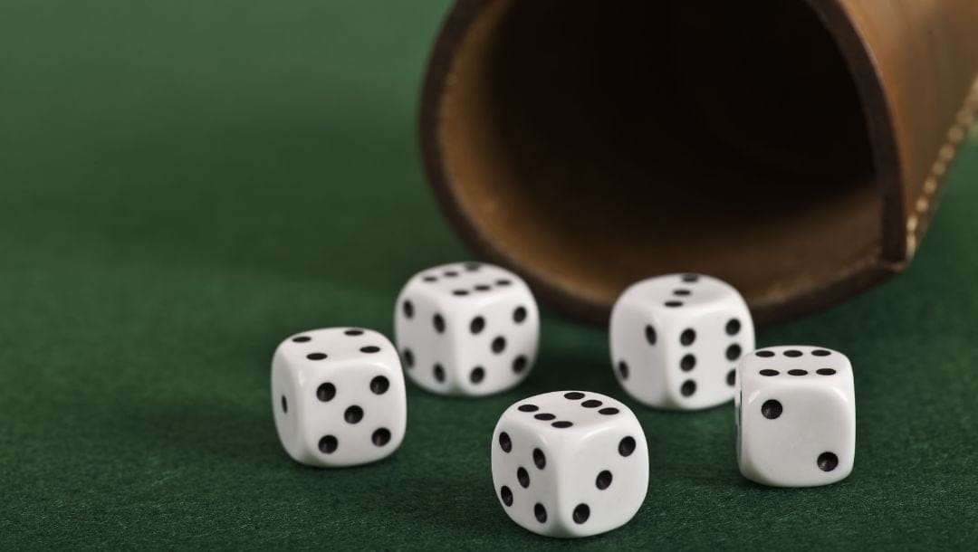 five regular six sided dice on a green felt surface with a leather cup behind them