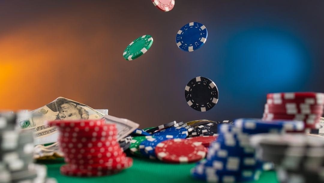 poker chips stacked and falling onto a green felt poker surface with dollar bills on it