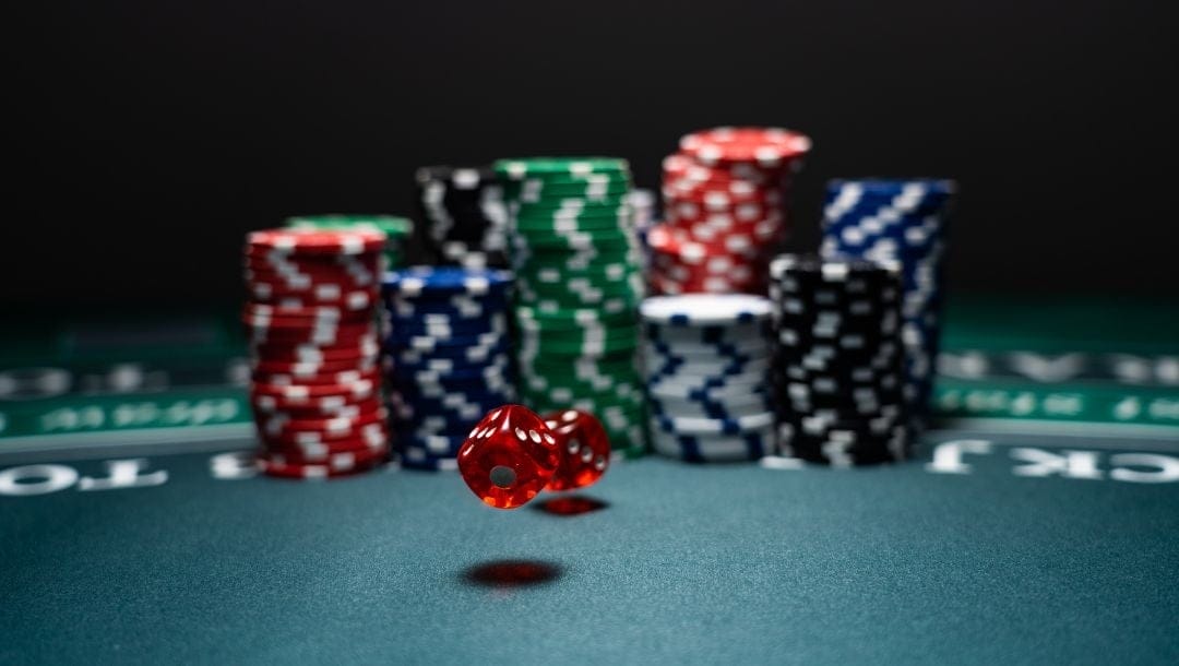 two red dice landing on a poker table surface in front of stacks of poker chips