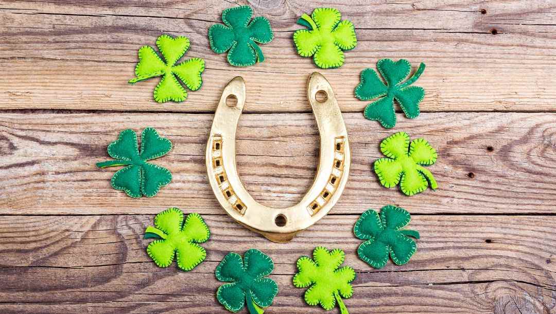 Header image, lucky horseshoe in the middle of a circle of felt four leaf clovers on a wooden surface