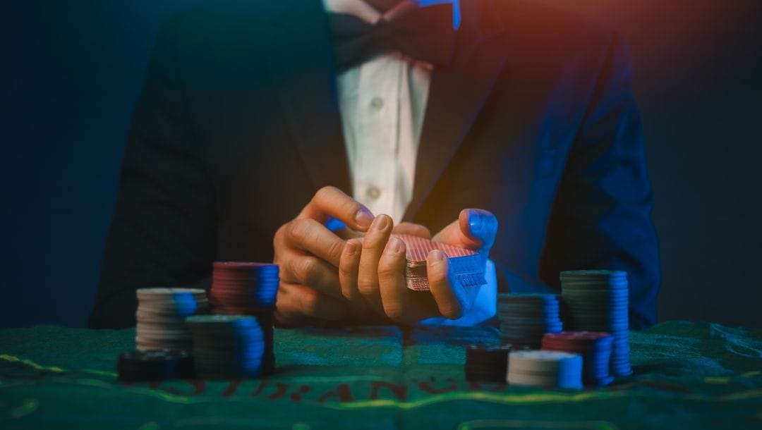 a man in a suit and bowtie shuffling cards at a poker table stacked with poker chips