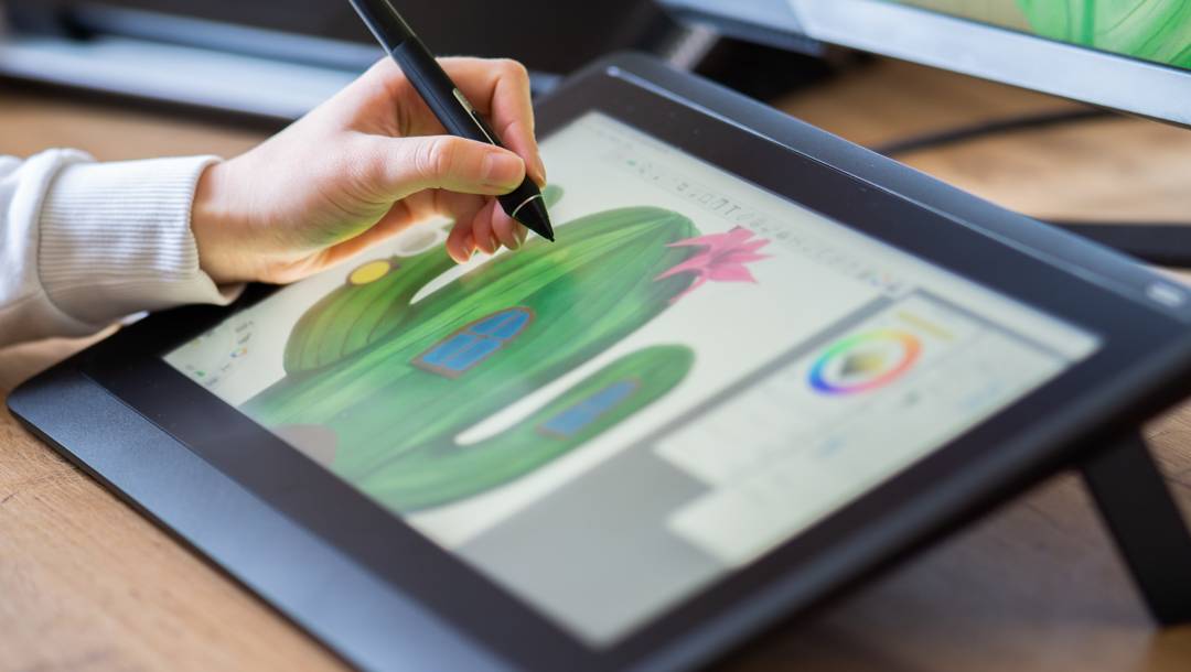 A person drawing a cactus with a window and a door using a stylus on a digital art tablet.