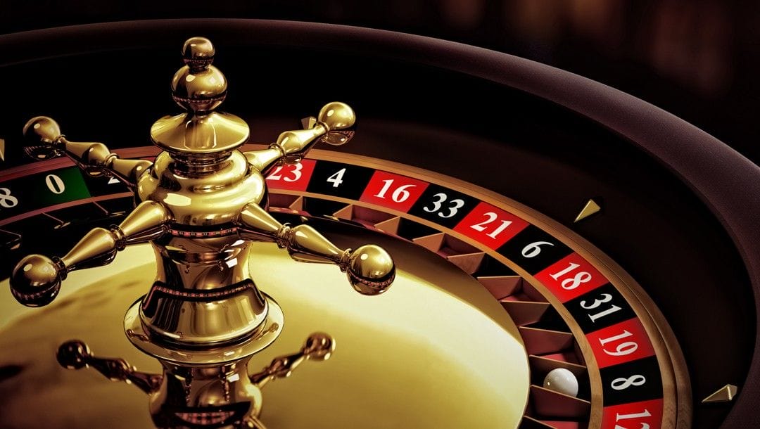 A close-up of a roulette wheel made from gold and wood with the classic red and black pockets. The roulette ball sits in the black eight pocket.