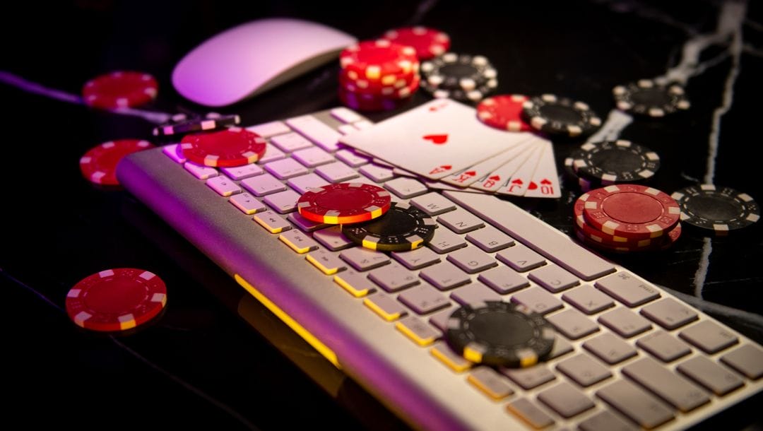 A mouse and keyboard surrounded by casino chips and a royal flush hand of playing cards