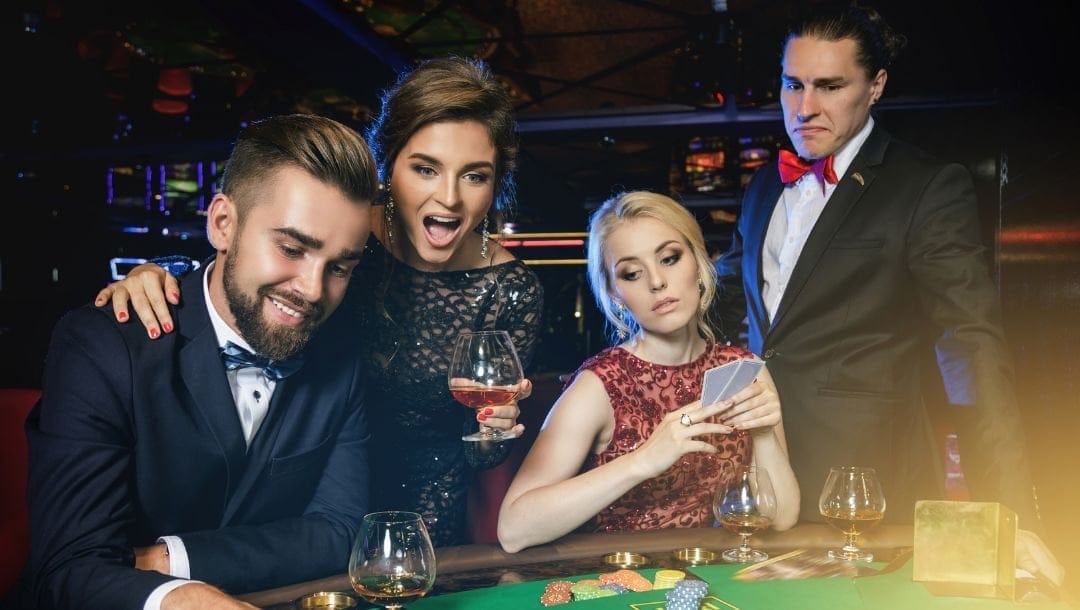 four friends, two couples, are sitting around a poker table in a casino playing poker, the one couple cheers and the other couple look disappointed as they have just lost the hand