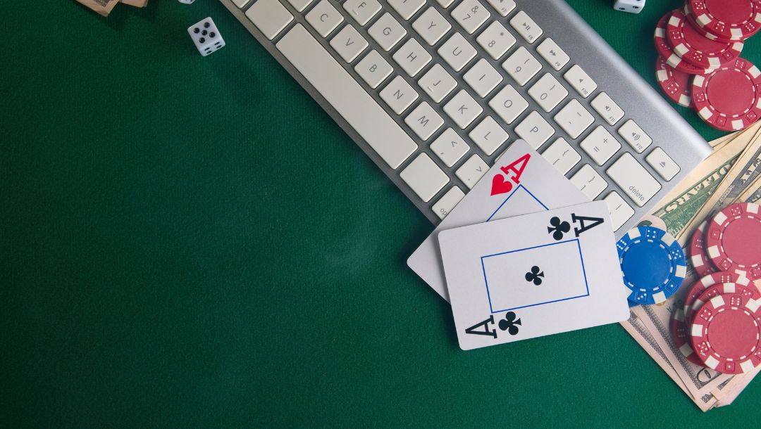 a pocket pair of ace playing cards on a computer keyboard on a green felt poker surface with poker chips, money and dice on it
