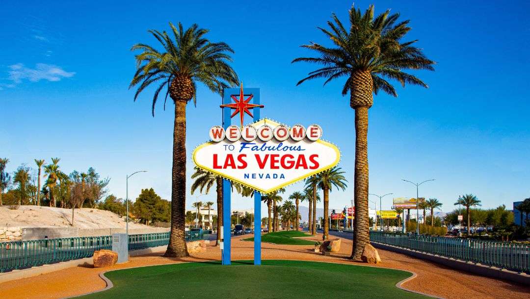 the famous “Welcome to Fabulous Las Vegas Nevada” sign in Las Vegas, USA with a palm tree on each side of the sign and blue skies above