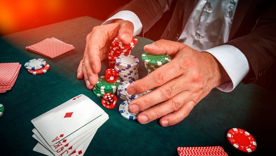a man putting his hands around stacks of poker chips on a green felt poker table with playing cards on it