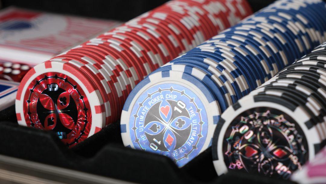 stacks of poker chips in a poker chip bank case with blurred playing cards and dice in the background