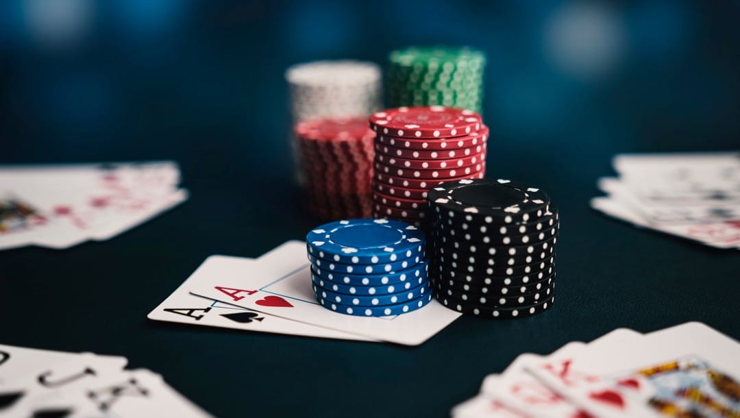 Stacks of poker chips on top of a pair of aces. Other poker hands are scattered around on the table.